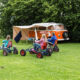 Pressearbeit in der Ferienzeit. Campingbus mit Zelt. Davor Kinder auf Gokarts auf Wiese.