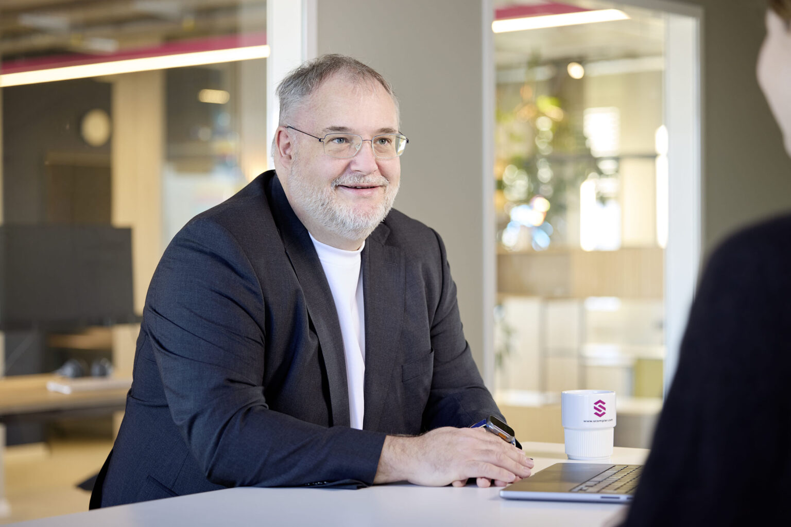 Der CEO von der Firma Scompler sitzt an einem Tisch und lächelt. Er ist im Gespräch.